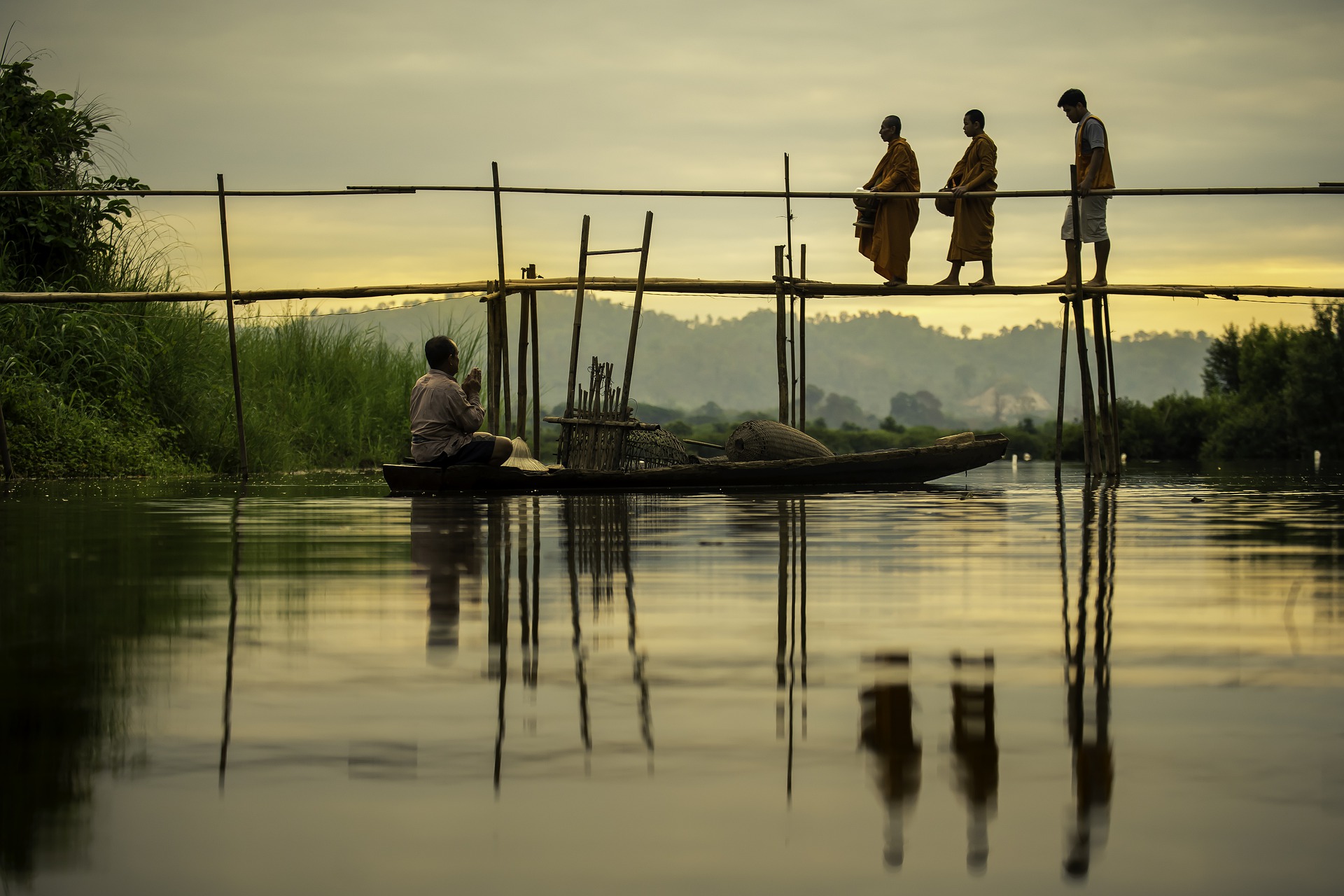 Monk with entourage walking over a bridge, while being prayed to by a fisherman in his dingy